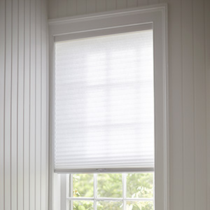 A Cellular Shade made of 3-4 Single Cell Light-Filtering in Lace covers a small window in a room with white wood paneling