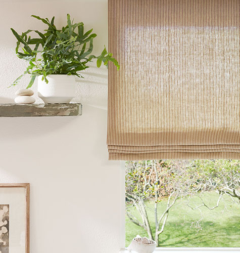 A close up of a Flat Roman Shade made of Surrey Stripe in Morel and Natural is next to a wood shelf with plants