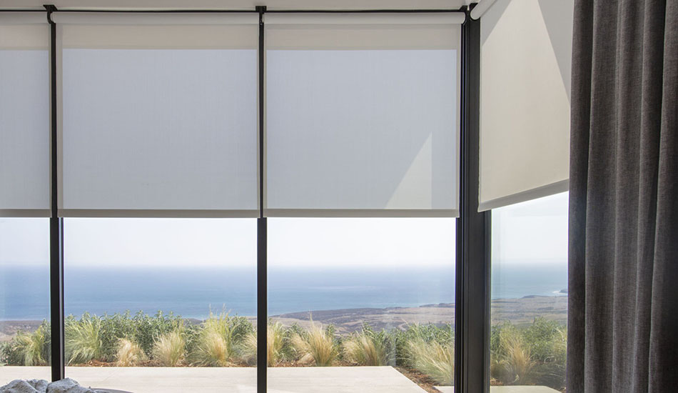 A bedroom features shades for sliding glass doors pulled halfway down to allow a view from the bed to the sea