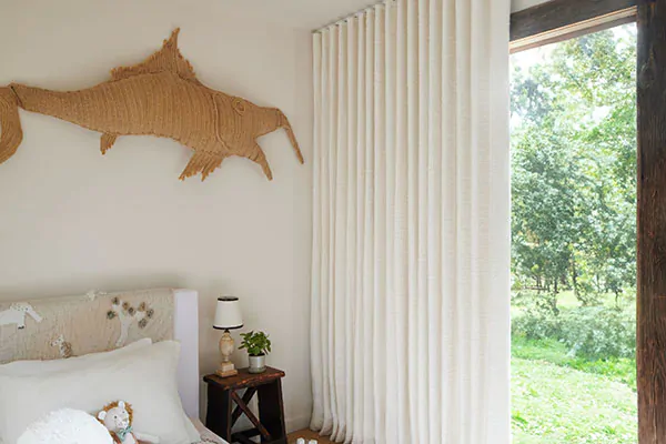 A bedroom with warm creamy tones features Ripple Fold Drapery made of Claude Stripe in Alabaster for texture and privacy