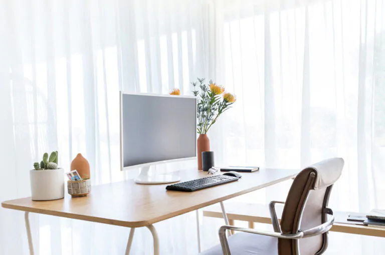 Home office curtains made of Sheer Elegance in Winter cover a corner window with a minimalist desk in front of it