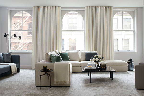A bright living room features curtains for arched windows made of Ripple Fold Drapery in Wool Flannel, Glacier