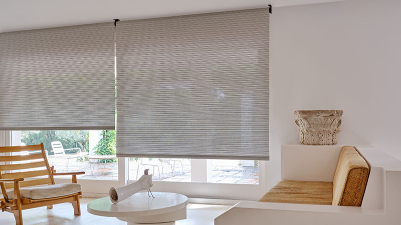 A minimalist living room with white and wood tones features Roller Shades made of Mesa Verde in Mist over sliding glass doors