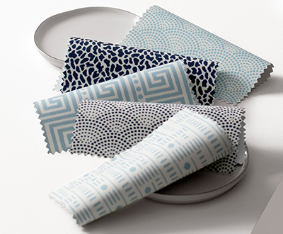 Swatches from Alexa Hampton's Design Collection for Roller Shades for windows lay folded on white saucers on a white table