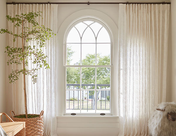 A nursery with warm white tones has neutral curtains of Novogratz Feather Palm Embroidery in Vintage Lace for a delicate look