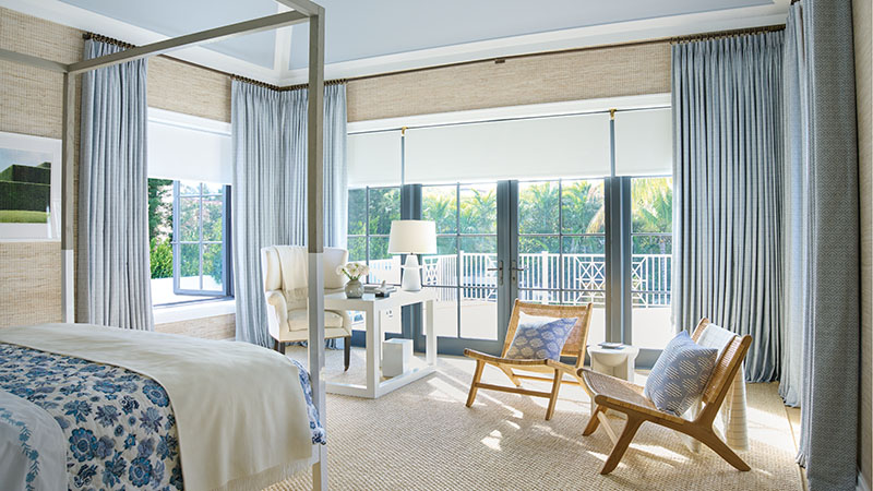 A coastal style bedroom has Tailored Pleat Drapery made of Vanda in Sky and Roller Shades made of Ava in Mist