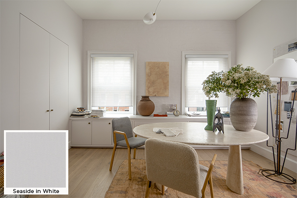 A creative workspace with a pot of flowers has Venetian Roller Shades for windows made of Seaside in White