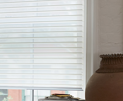 Venetian Roller Shades for windows made of Seaside in White cover a window with a pile of books and jar in front of it