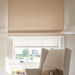 An inviting playroom has a Waterfall Woven Wood Shade made of Somerset in Cloud over a tall window behind a wingback chair